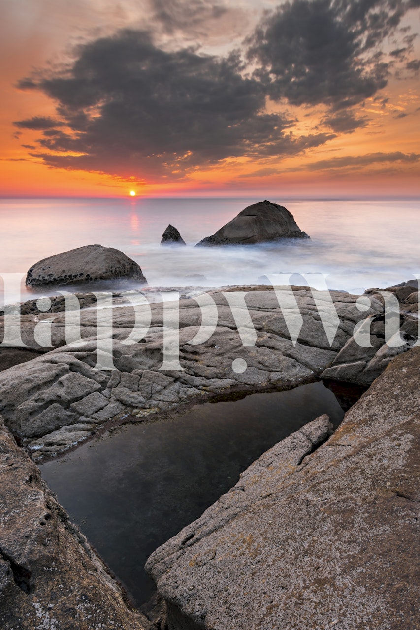 Sunset over the ocean with rocks and reflection. Orange and blue coastal wallpaper.