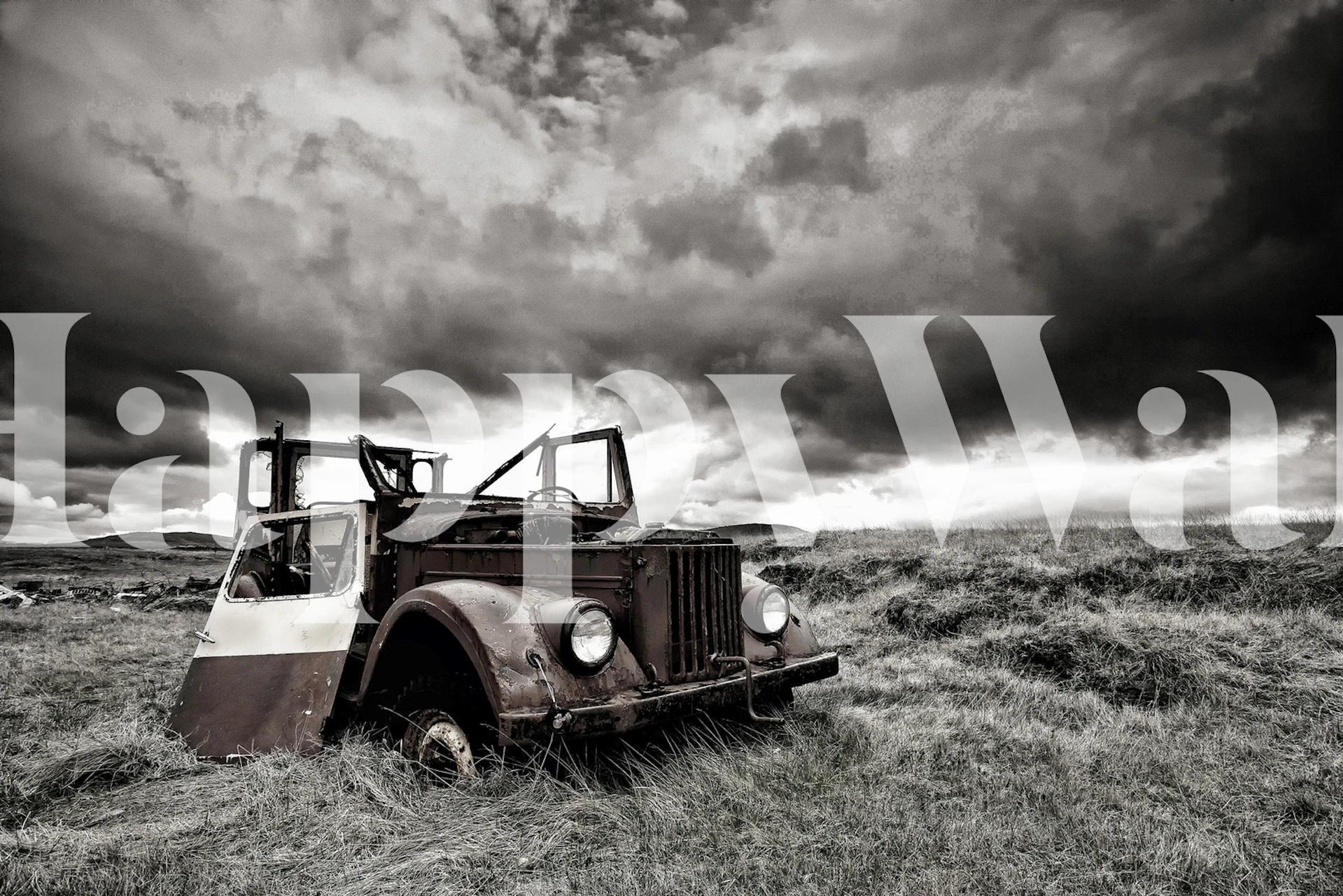 Vintage black and white wallpaper featuring an abandoned vehicle in a field under cloudy skies