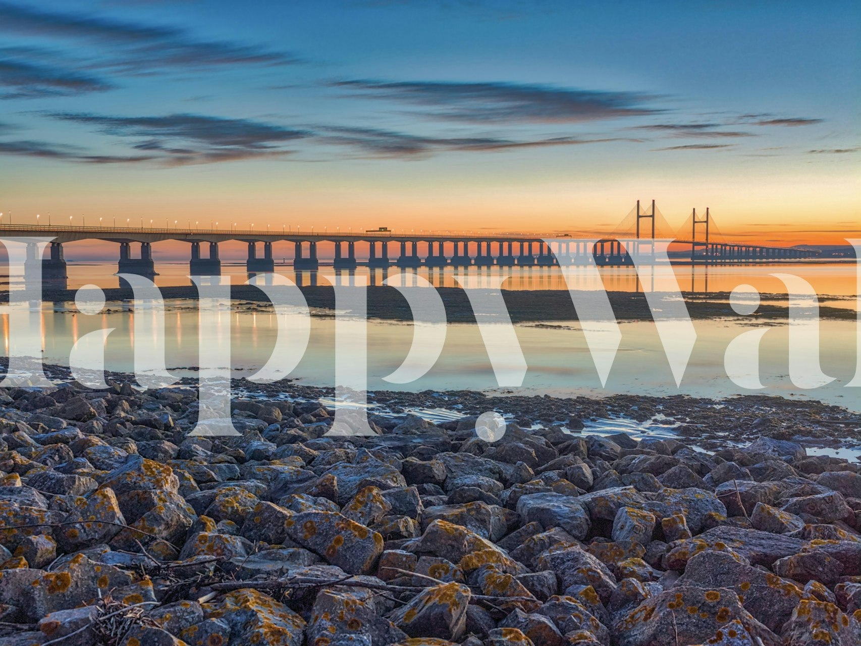Scenic view of a river and bridge at sunset with rocky shore wallpaper