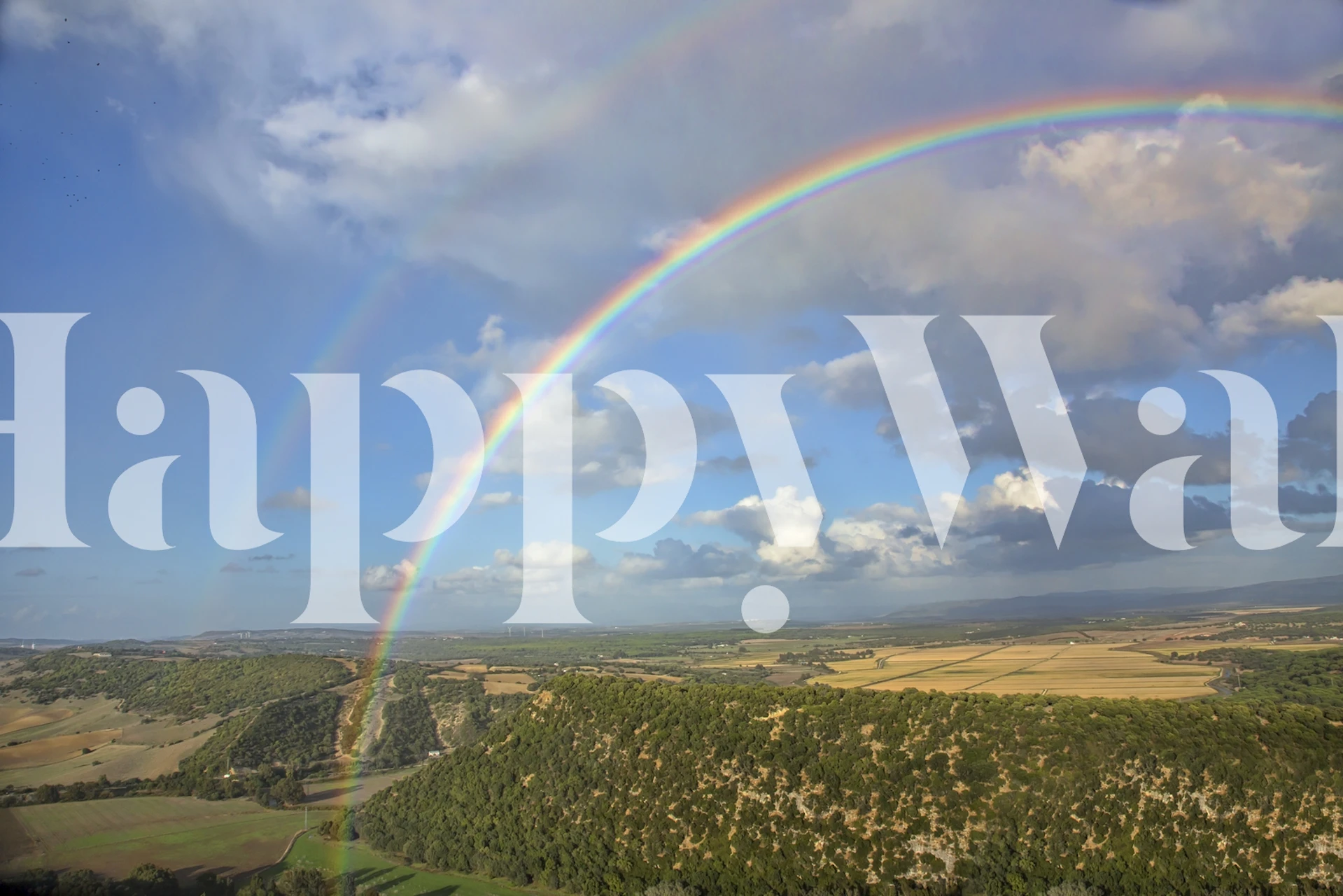 Rainbow arch over green hills under blue sky wallpaper