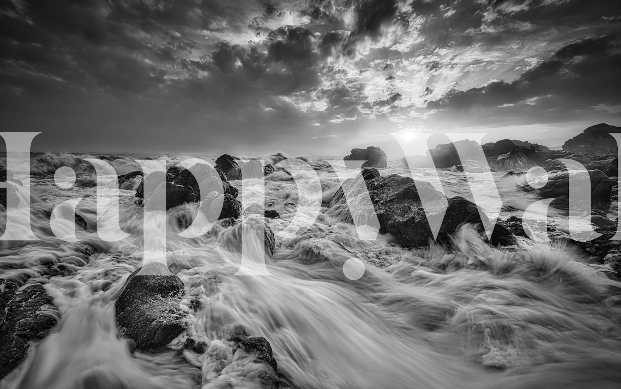 Fotomural monocromático de um mar agitado ao pôr do sol com ondas quebrando sobre rochas