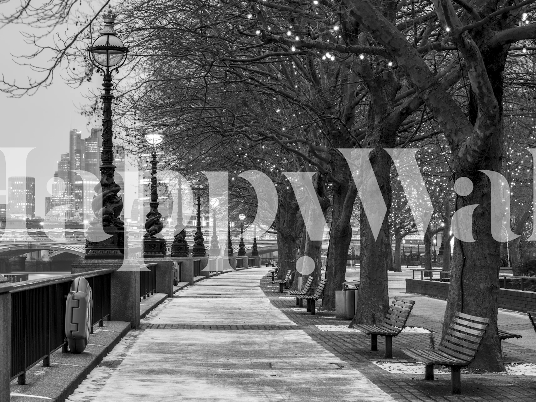 Black and white river promenade scene with trees, benches, and city skyline wallpaper
