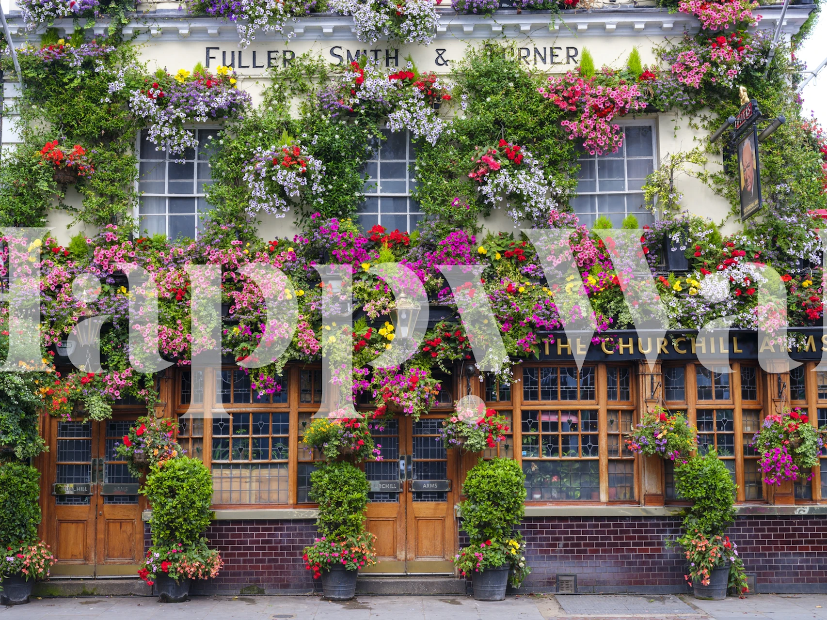 The Churchill Arms pub wall mural with lush hanging flower baskets and classic British facade
