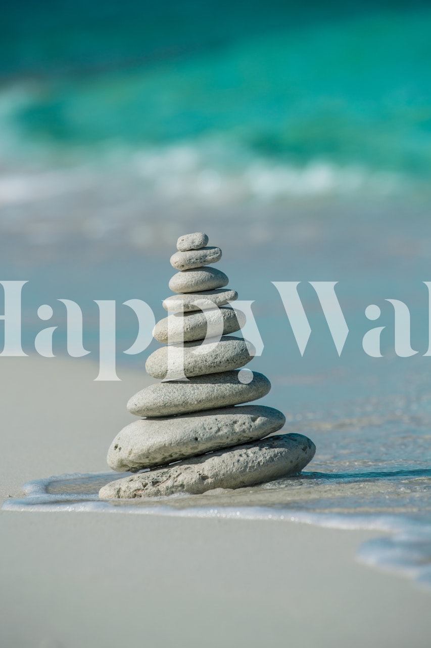 Stacked stones on a sandy beach with blue waves wallpaper