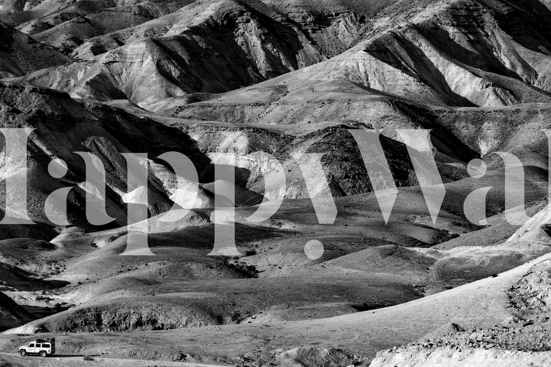 Black and white desert landscape wallpaper showing rugged hills and a vehicle