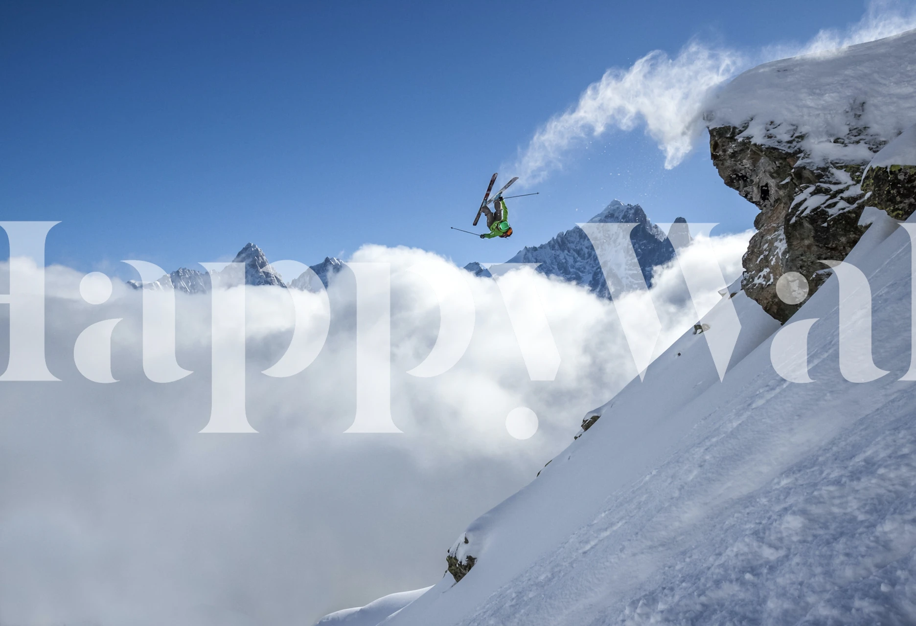 Skier performing a loop on snowy mountain with clouds below