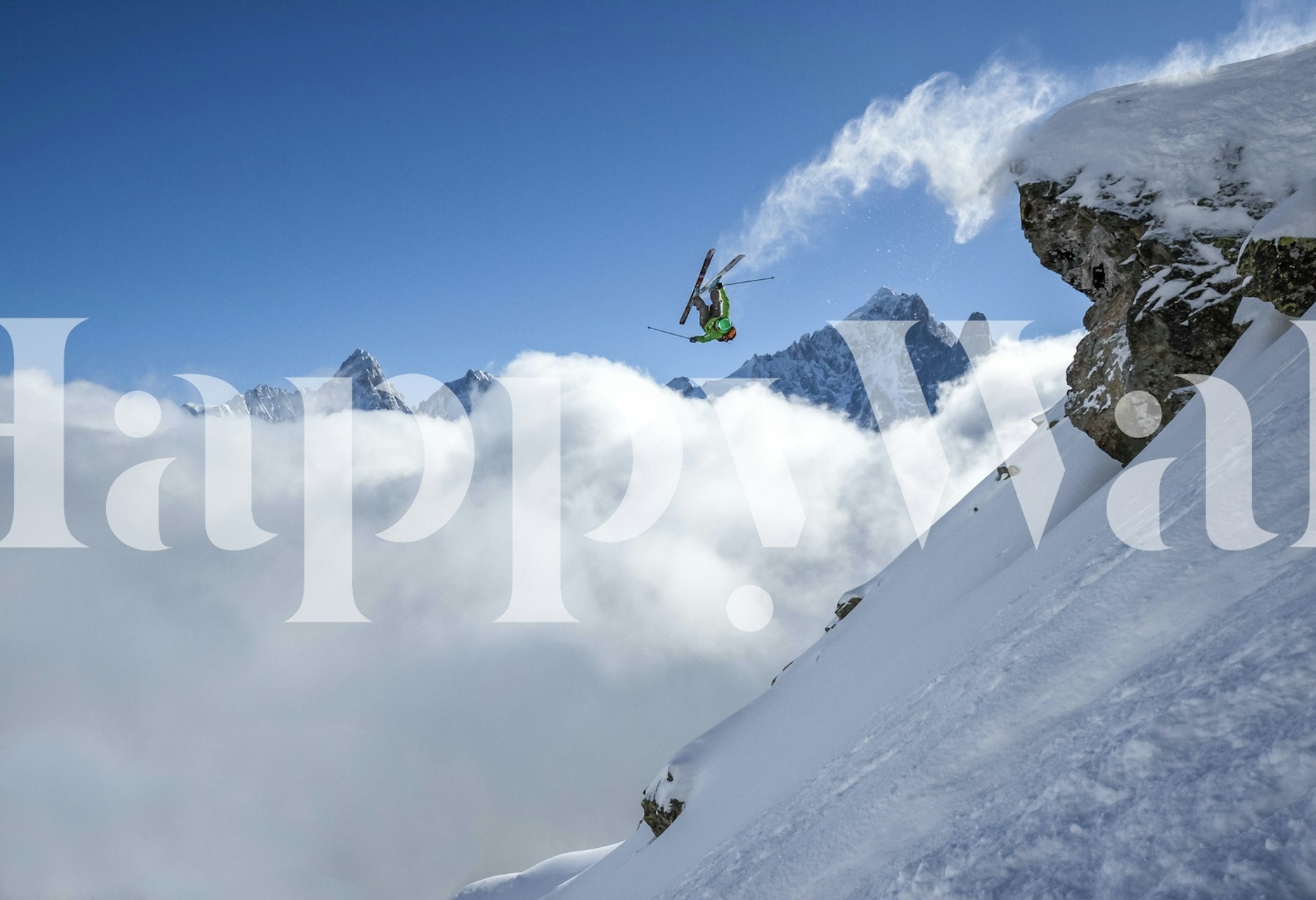 Skier performing a loop on snowy mountain with clouds below