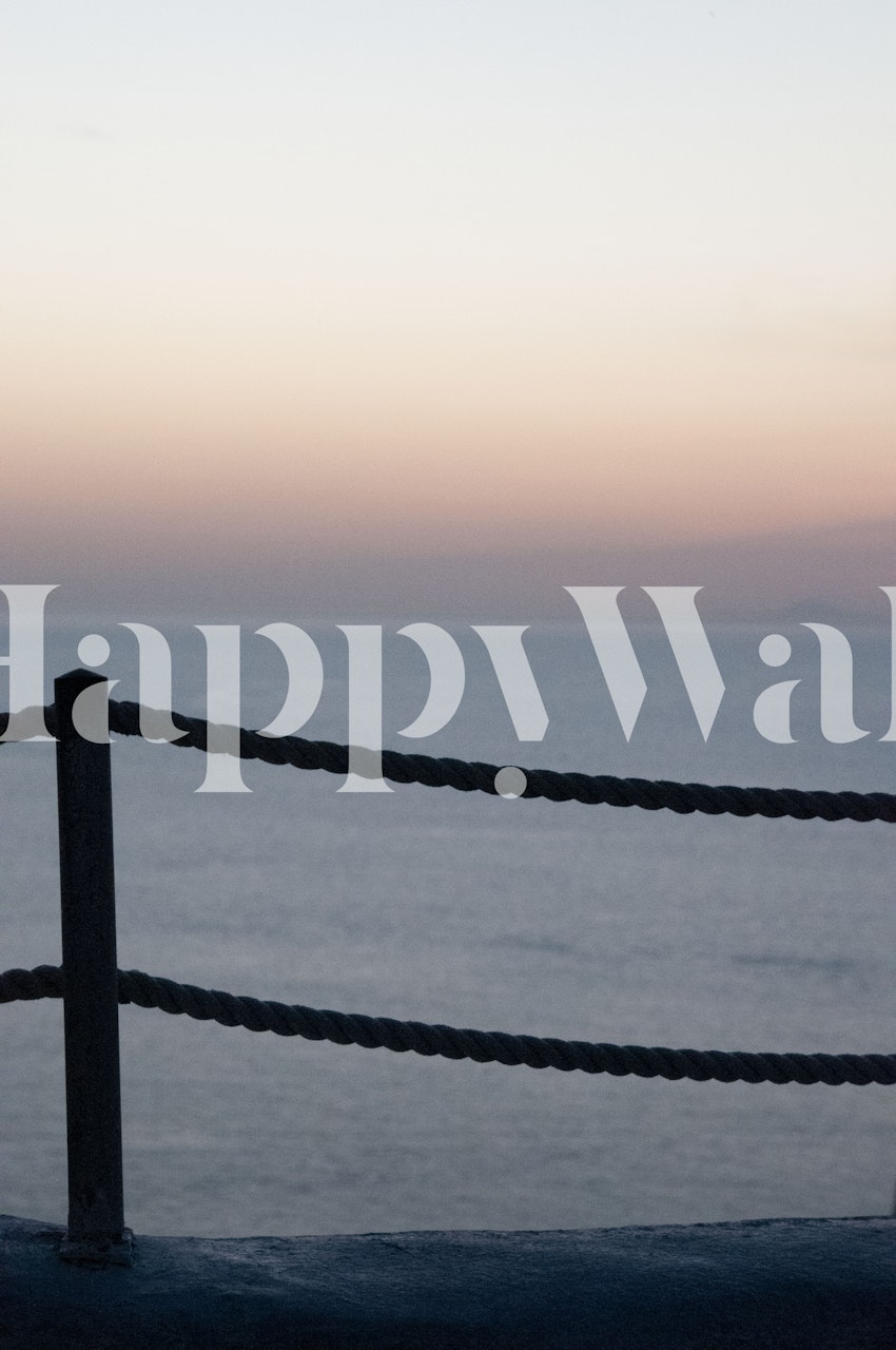 Silueta západu slunce na Santorini s provazovým plotem a nástěnnou malbou klidného moře