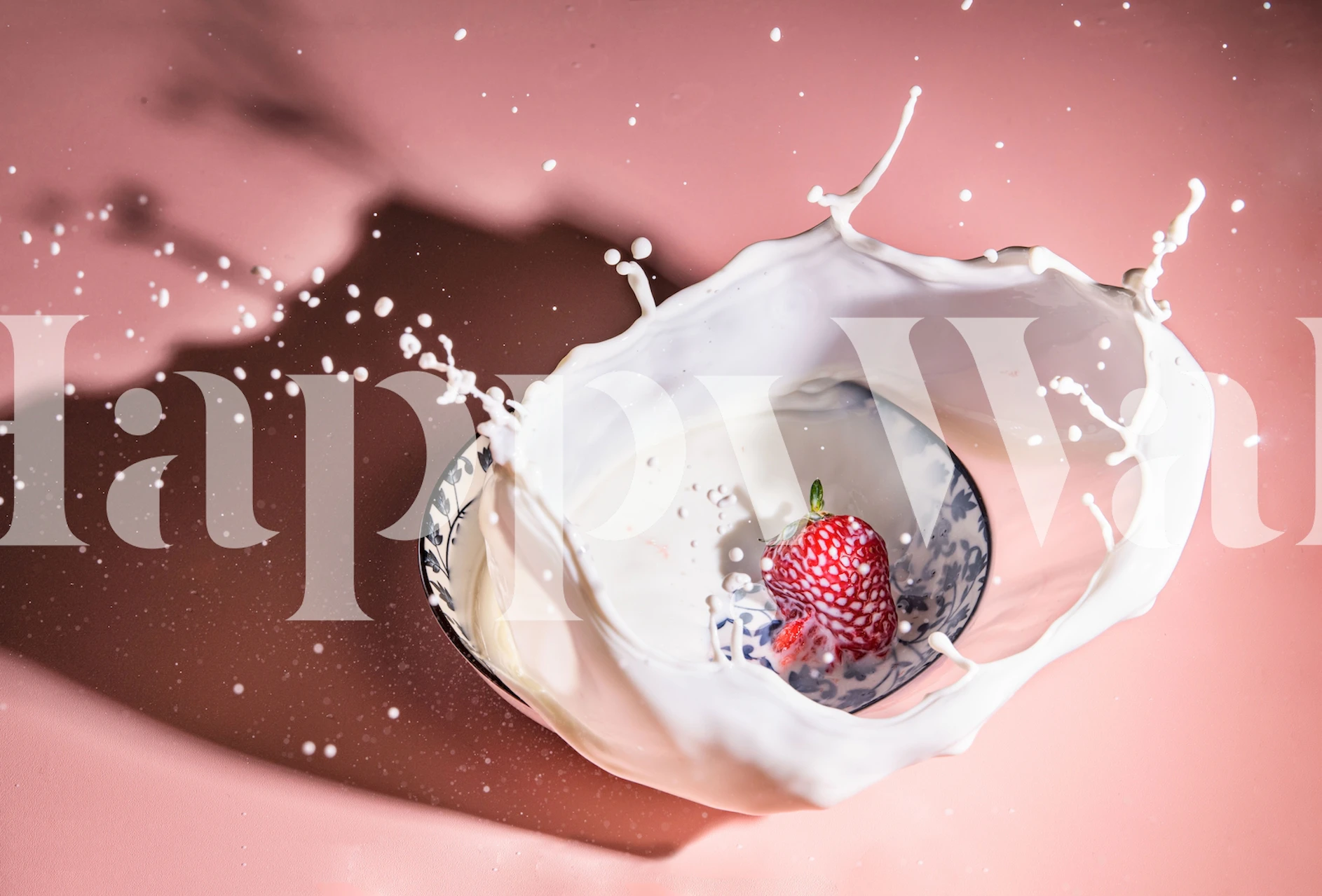 Mansikka, joka luo roiskeita maitoon vaaleanpunaisella taustalla.