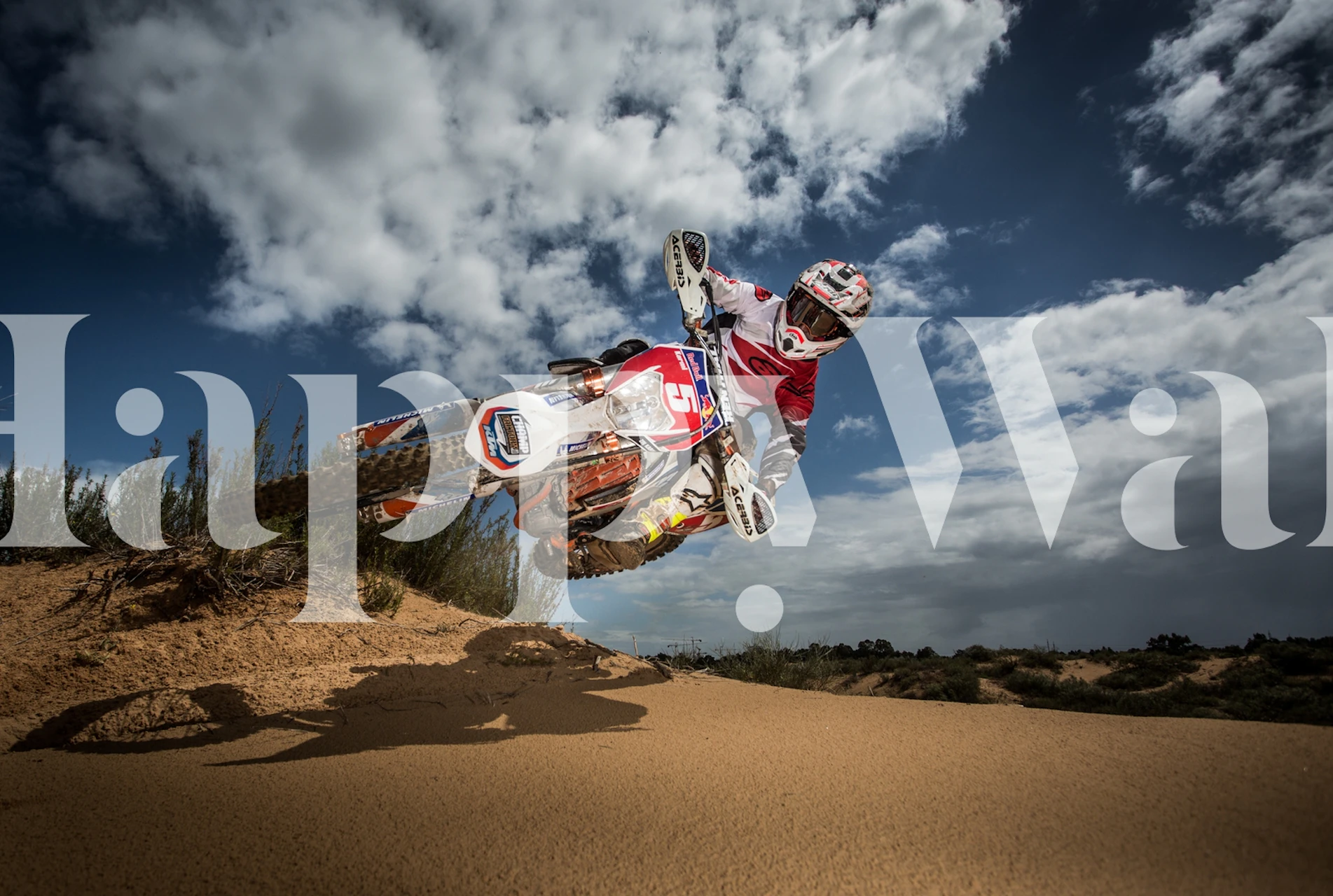 Motocross rider in mid-air over sandy terrain against a dramatic sky wallpaper