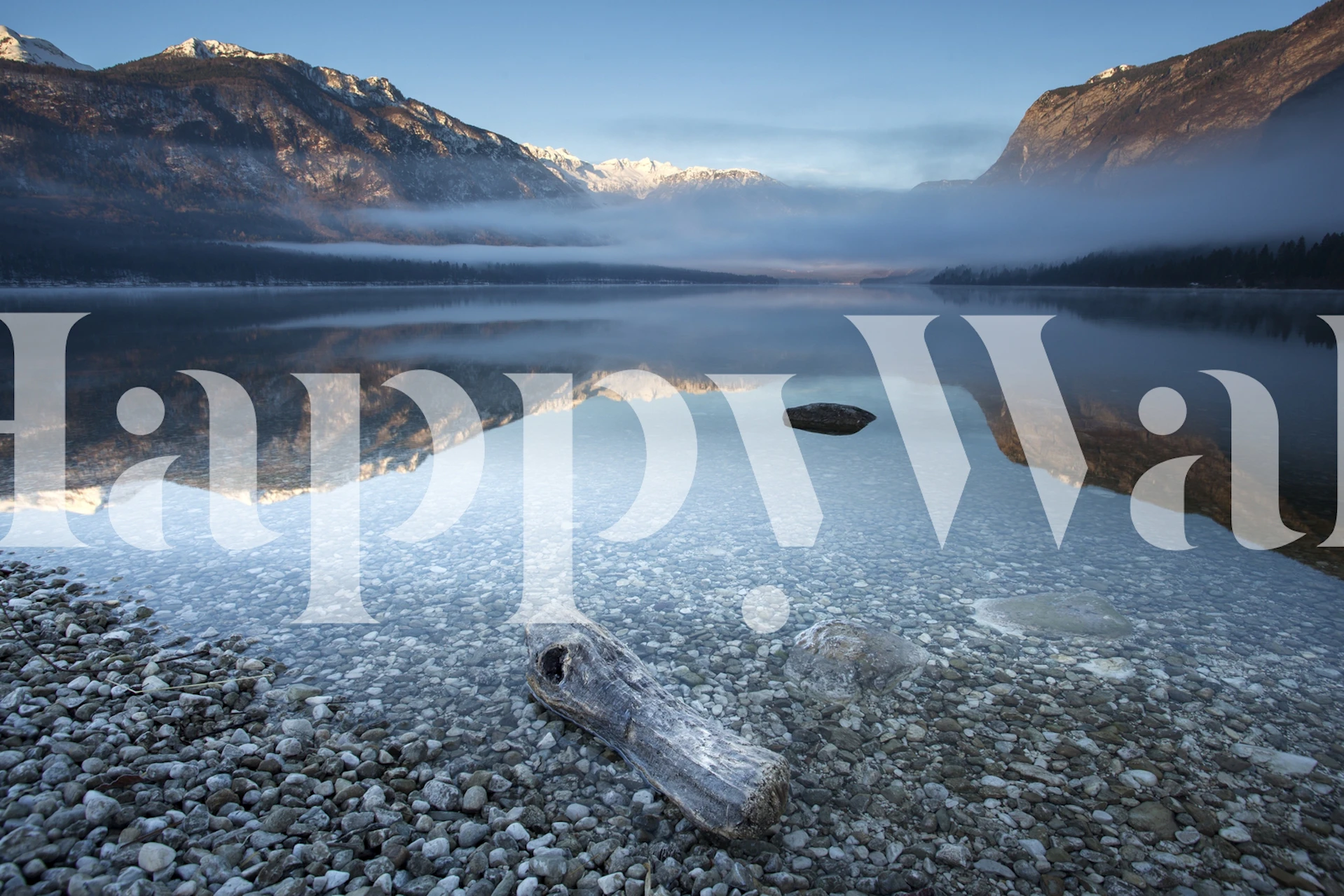 A tranquil mountain lake scene wallpaper featuring blue hues, stone shore, and reflections of surrounding mountains.