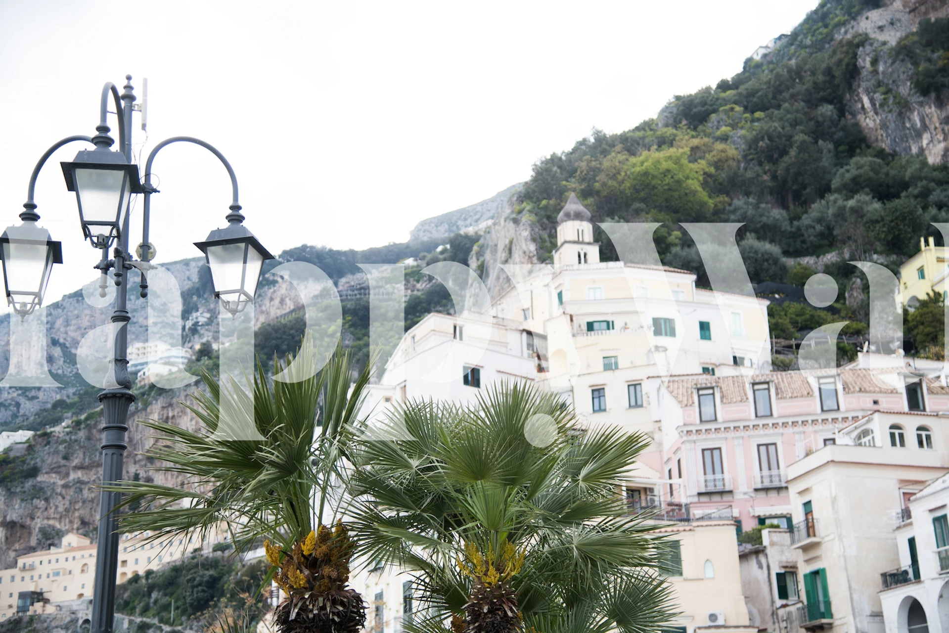 Um mural panorâmico da costa de Amalfi com edifícios em tons pastéis, vegetação e luminárias de rua.