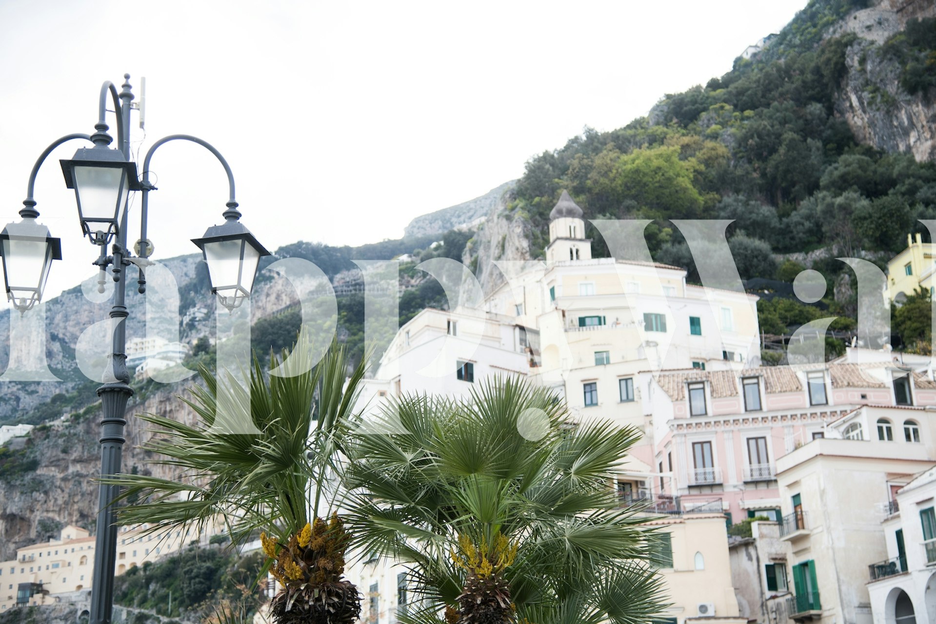 A scenic wall mural of the Amalfi coast with pastel buildings, greenery, and street lamps.