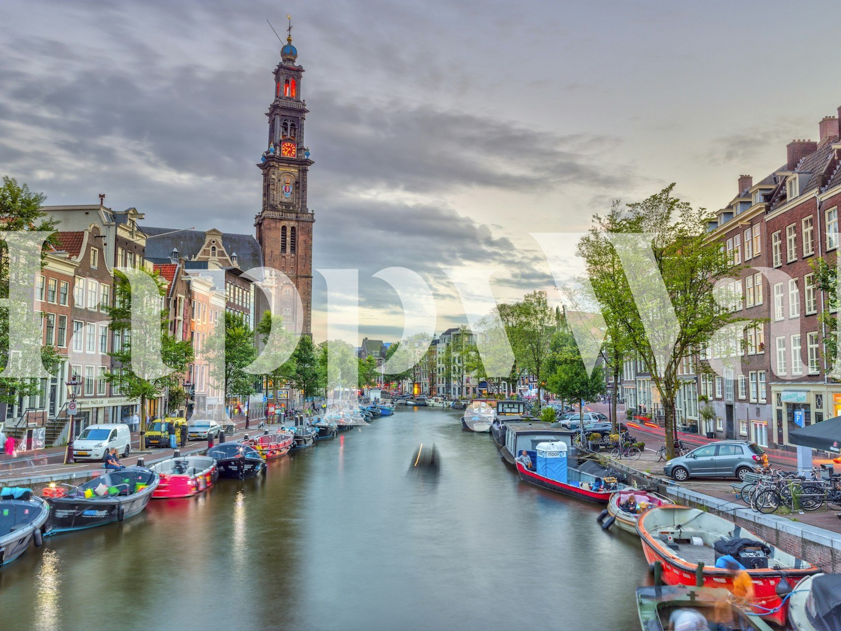 A picturesque canal scene with boats and trees, colorful buildings and a clock tower wallpaper