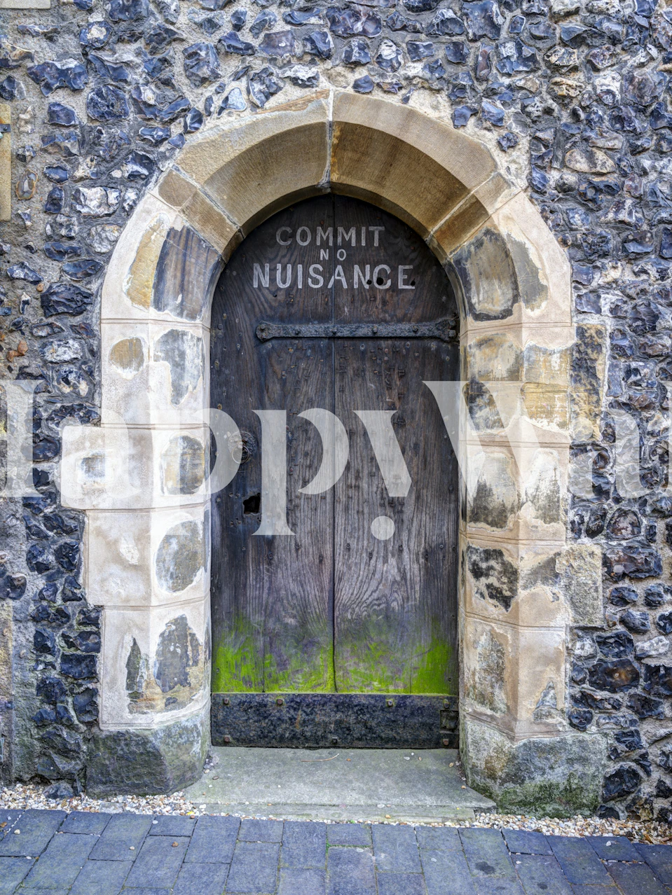 Weathered stone wall with an arched doorway and text 'COMMIT NO NUISANCE' wallpaper