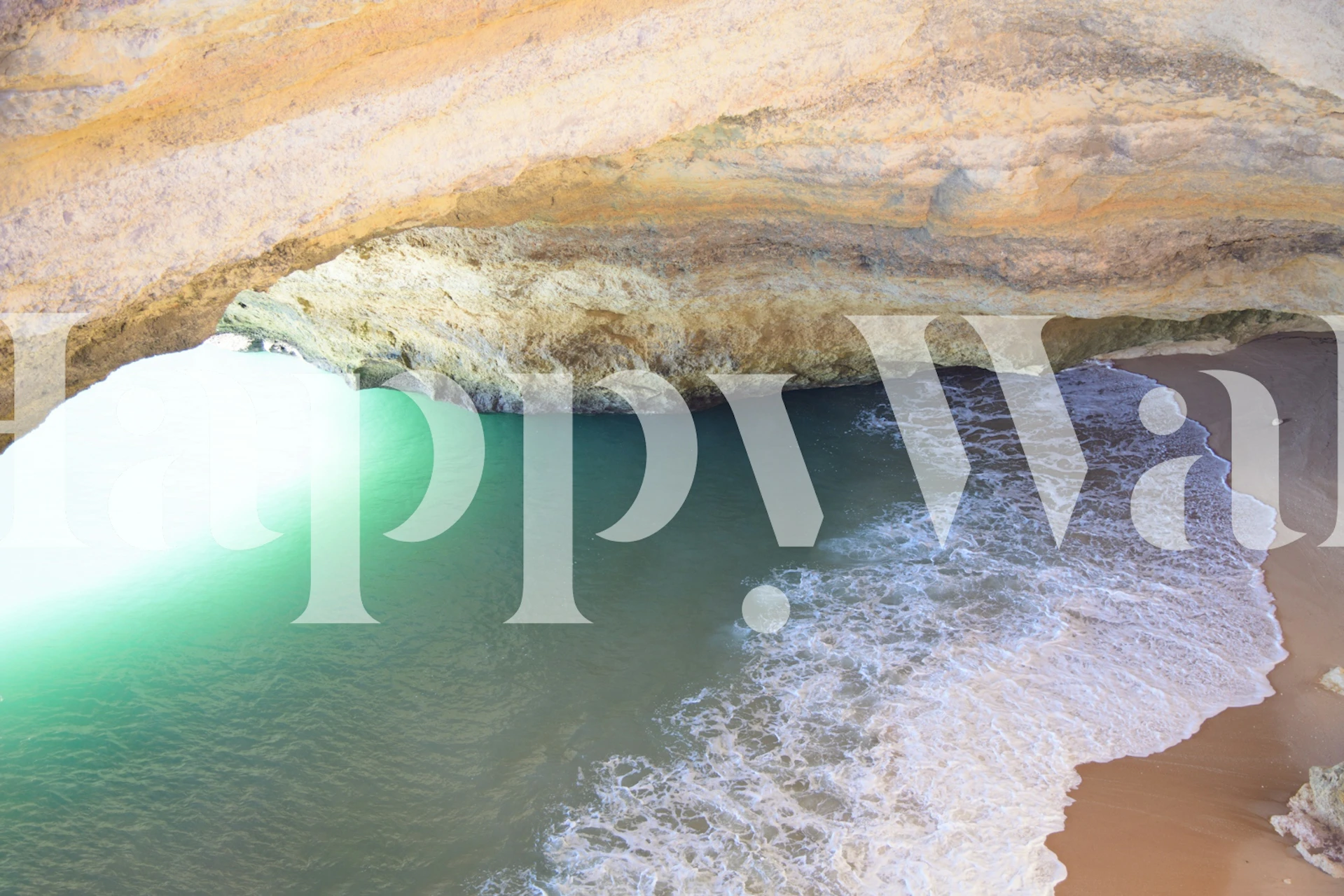 Turquoise ocean waves and sandy beach under a rock cave wallpaper