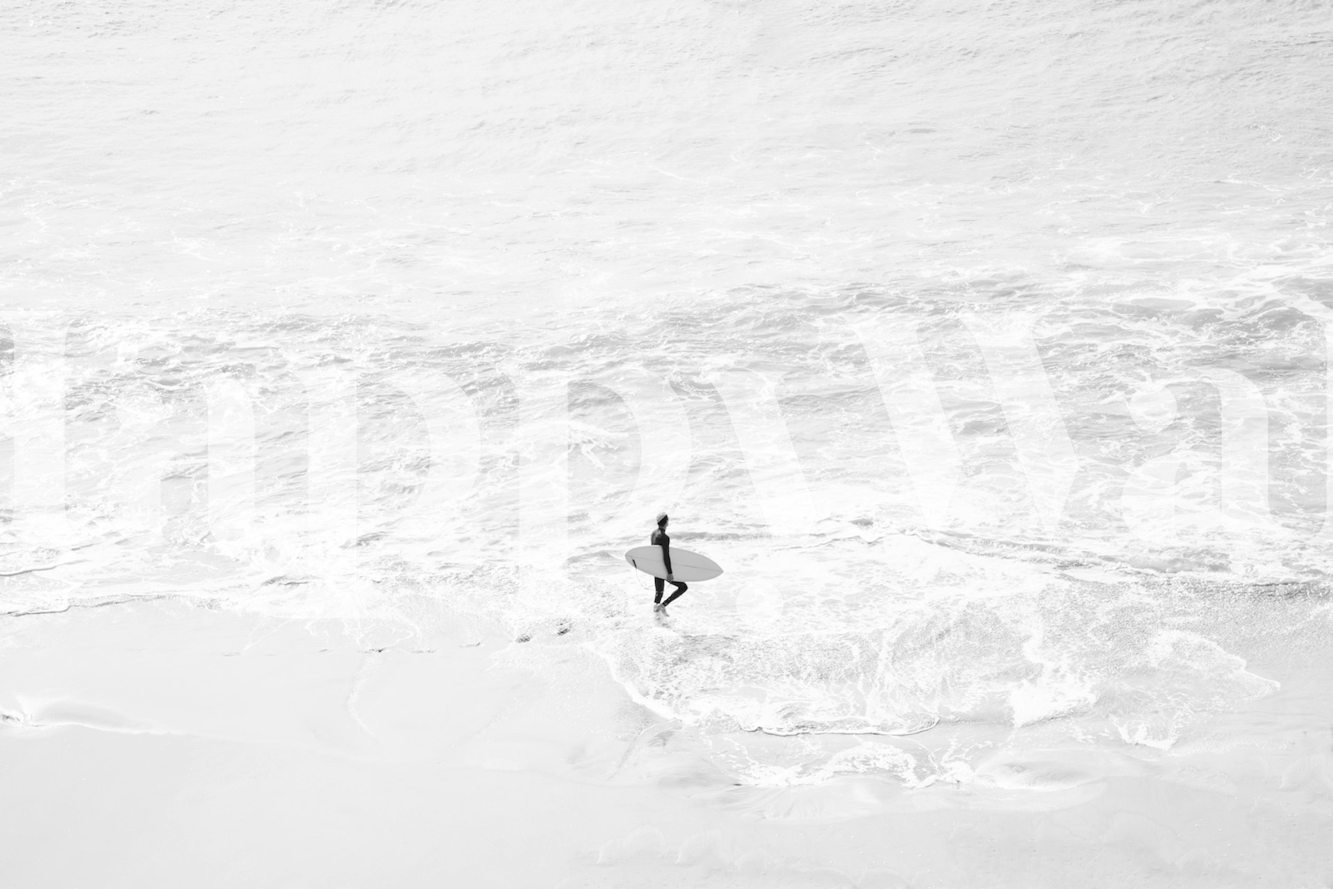 Surfer standing in ocean waves on a beach black and white wallpaper
