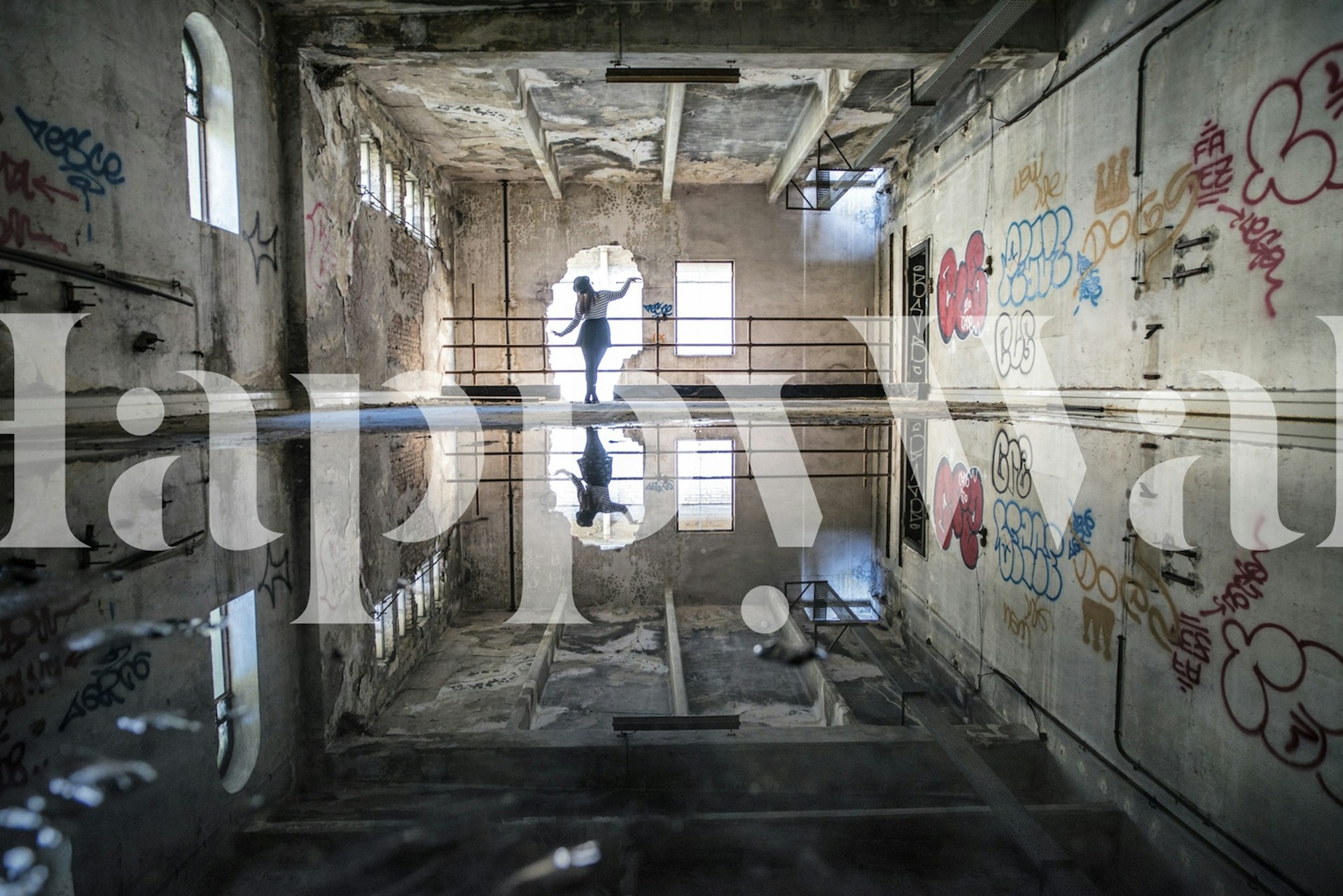 Mural de una bailarina en una habitación iluminada por el sol y cubierta de graffiti con un piso reflectante que crea una imagen especular