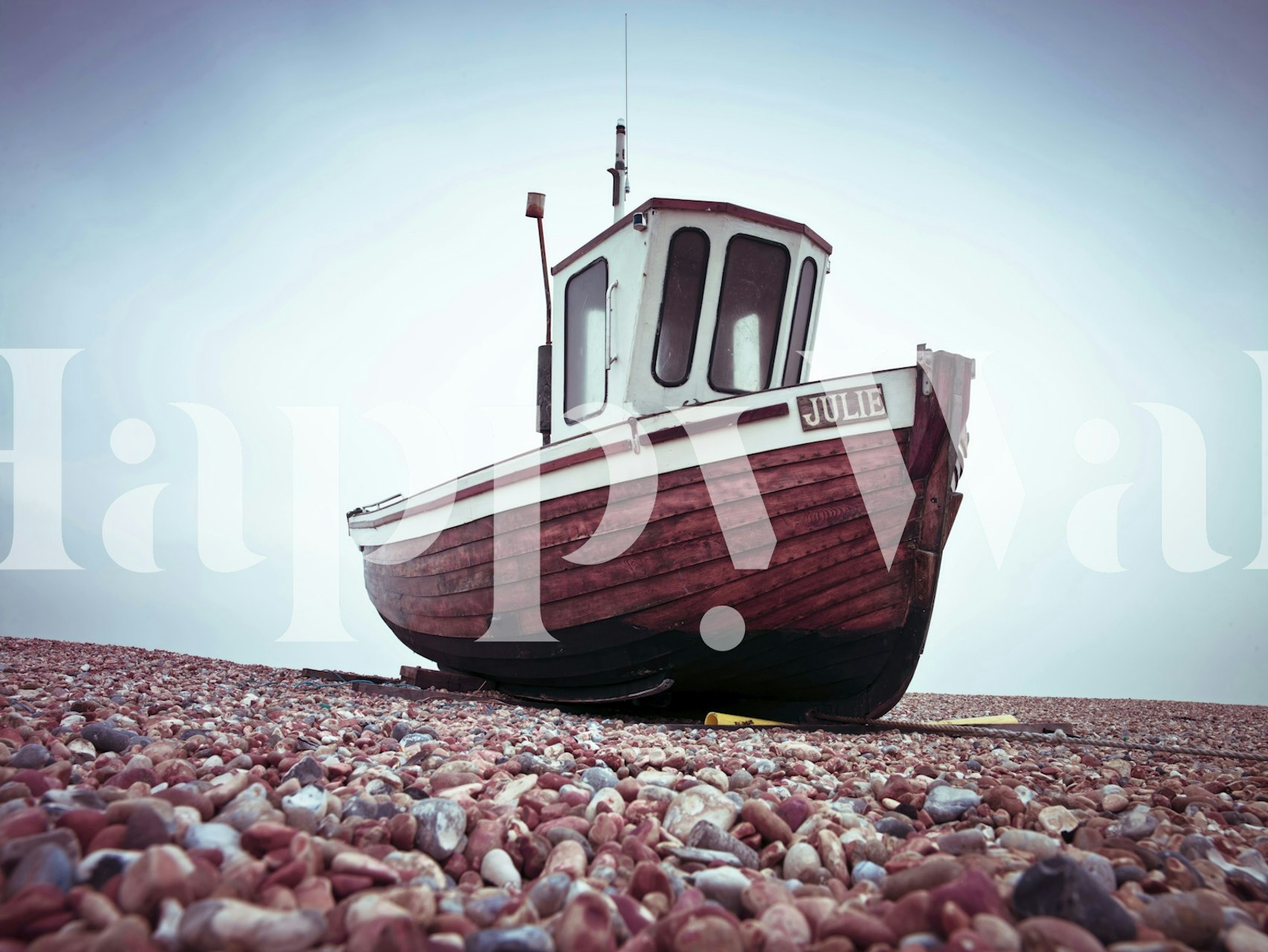 Wall mural of a lone boat on a pebbled beach with overcast skies evoking tranquility and solitude.